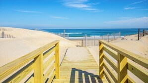A wooden boardwalk leading to a sandy beach with a clear blue sky and ocean in the background. - 7050 Sailor's Rest at Nags Head * Oceanfront (Nags Head)