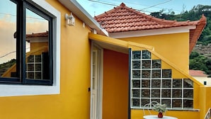 A yellow building with a tiled roof, a window, and a small patio area with a table and chairs. - Casa do Perestrelo - Guest House (Machico)