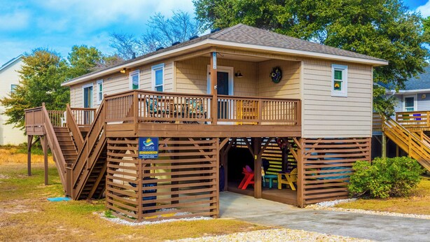 A two-story wooden building with a deck and a staircase leading to an upper level. - Home Sweet Helga: Beach & Sound Access (Kill Devil Hills)