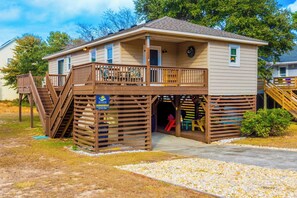 A two-story wooden building with a deck and a staircase leading to an upper level. - Home Sweet Helga: Beach & Sound Access (Kill Devil Hills)