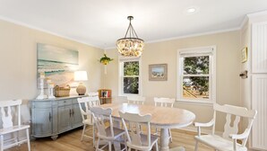 A dining room with a round table, white chairs, a blue cabinet, and a chandelier. - Home Sweet Helga: Beach & Sound Access (Kill Devil Hills)