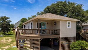 A two-story wooden cabin with a balcony, a small porch, and a garage entrance. - Home Sweet Helga: Beach & Sound Access (Kill Devil Hills)