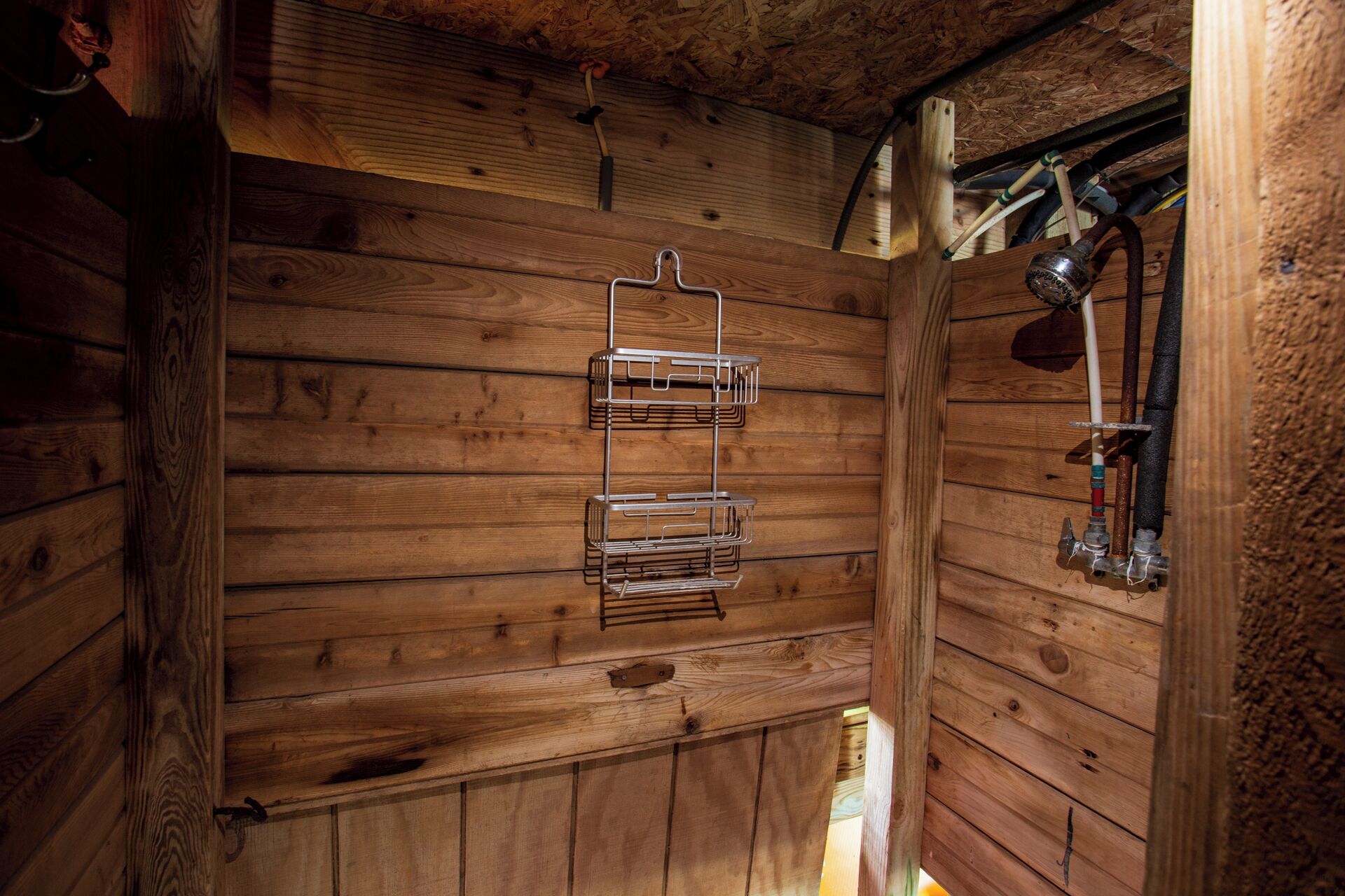 Een houten interieur met een metalen rek aan de muur en zichtbare leidingen.