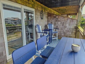 A covered patio with a table and chairs, a small table with a candle, and a sliding glass door leading to a backyard. - Cozy 1BR Soundfront Condo | King Bed & Sunset Views (Avon)