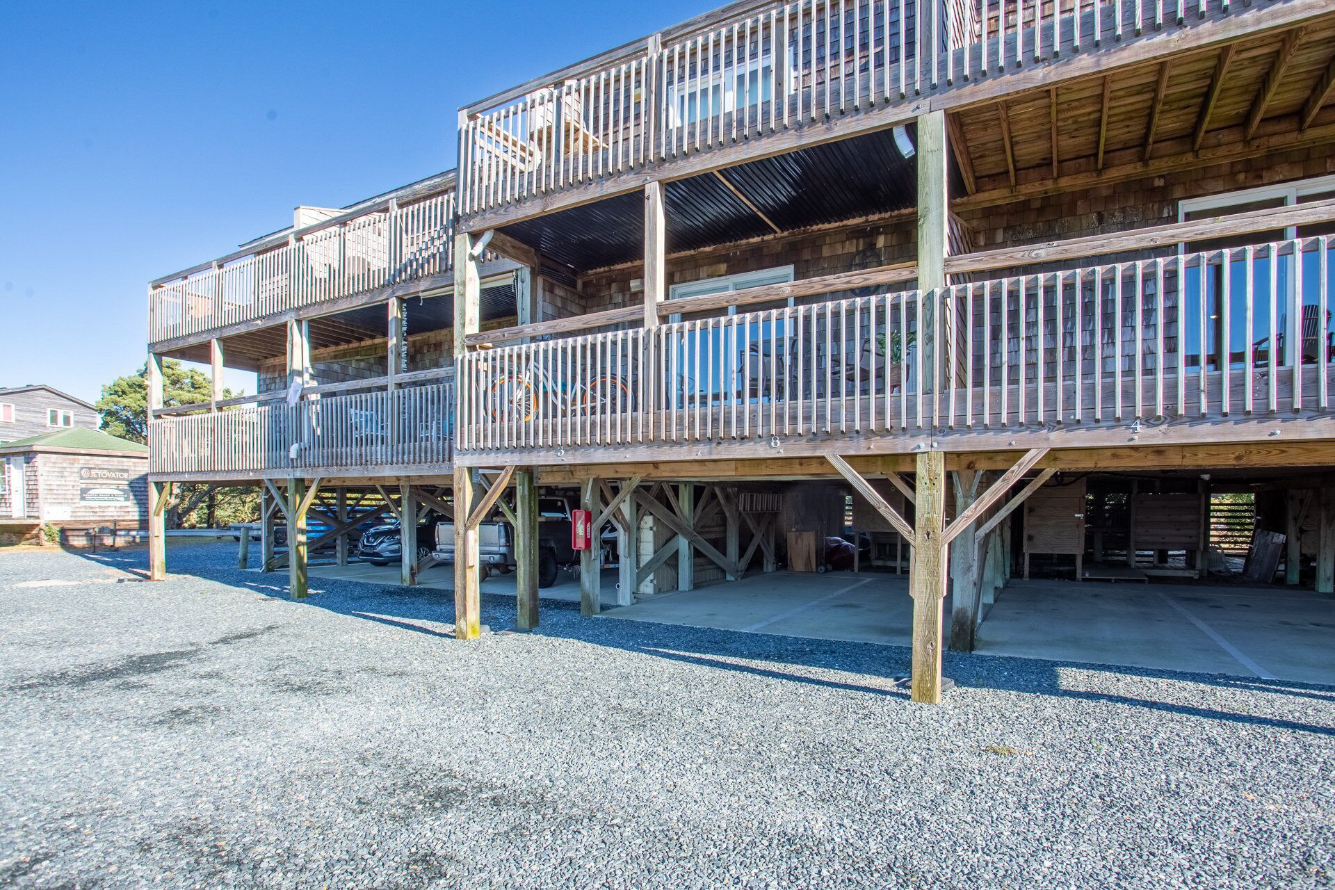 A multi-story wooden building with balconies, a gravel ground, and a clear blue sky.