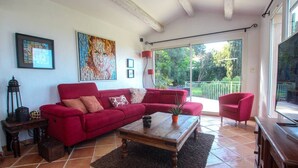Ein Wohnzimmer mit einem roten Sofa, einem Holztisch und einem großen Fenster mit Blick auf Grünflächen.