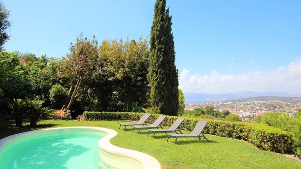 Ein Pool mit Liegestühlen, umgeben von Grünpflanzen und mit Blick auf eine ferne Skyline.
