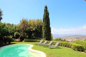 Ein Pool mit Liegestühlen, umgeben von Grünpflanzen und mit Blick auf eine ferne Skyline.