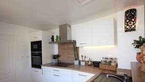 Eine moderne Küche mit weißen Schränken, einem eingebauten Backofen, einer Edelstahl-Spüle und einer Wandleuchte.