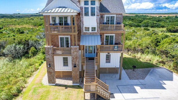 A multi-story house with a balcony on each floor, surrounded by a natural landscape.
