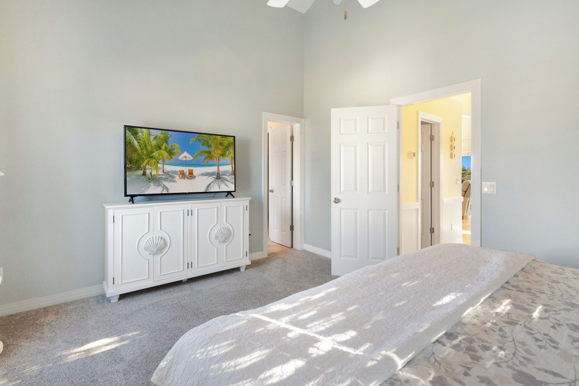 Un dormitorio con una cama, un televisor sobre un aparador blanco y una puerta que da a otra habitación.