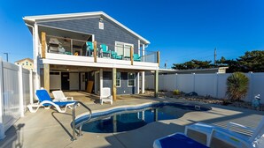 A two-story house with a swimming pool, a covered patio, and a fenced backyard.