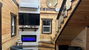 Een gezellige kamer met houten wanden, een open haard, een flatscreen-televisie en twee zwarte stoelen.