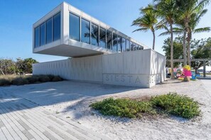 Un edificio moderno con una sección voladiza, suelo arenoso y un cartel que dice "SIESTA BEACH".