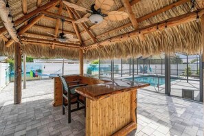 Un espacio exterior cubierto con piscina, mobiliario de madera y techo de paja.