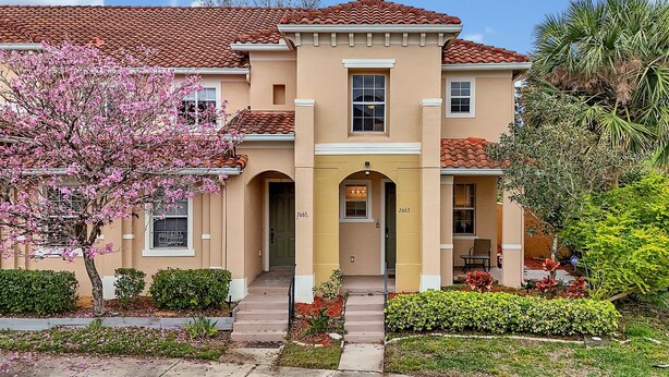 A two-story house with a beige facade, red-tiled roof, and a front porch with steps leading to the entrance. - Minutes to Magic! Walt Disney World Awaits (Kissimmee)