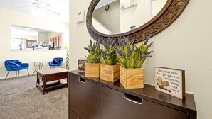 A room with a wooden dresser, a mirror, and three wooden boxes with plants. There are two blue chairs and a small table in the background. - Minutes to Magic! Walt Disney World Awaits (Kissimmee)