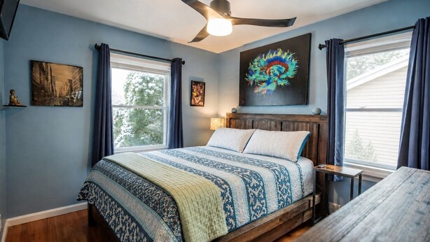 A bedroom with a bed, a ceiling fan, a window with curtains, and artwork on the wall. - Peaceful Pretty Art and Cinema Reclining Couches (Ferndale)