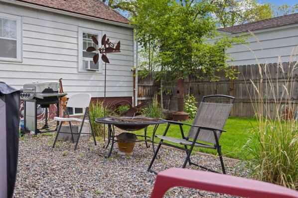 A backyard with a grill, chairs, a wind chime, and a wooden fence. - Bo’s 3BR Retreat • Hot Tub • Sauna • Den Suite (Billings)