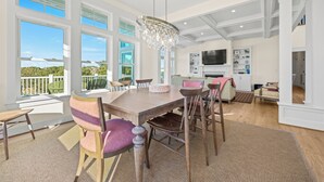 Une salle à manger spacieuse, dotée d’une grande table, de chaises et d’un lustre. De grandes fenêtres offrent une vue sur la verdure environnante.