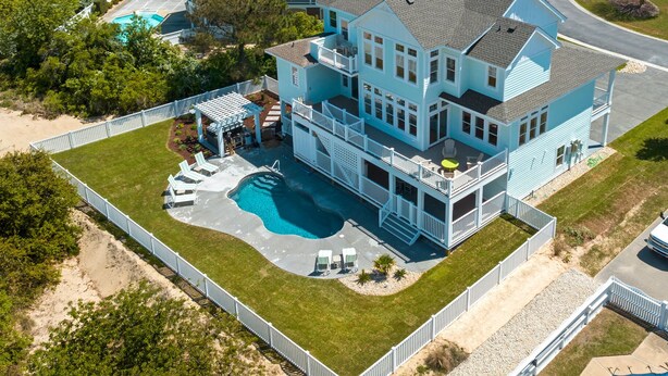 Une grande maison à deux étages, dotée d’une piscine, de plusieurs balcons et d’un patio couvert.