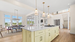 Une cuisine spacieuse dotée d’un grand îlot central, de luminaires suspendus et offrant une vue sur l’extérieur.