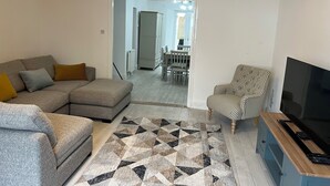 A living room with a sectional sofa, a striped armchair, a TV, and a geometric rug. - Fully refurbished 4 bed home in heart of West Looe (Looe)
