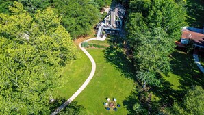 An aerial view of a house surrounded by lush greenery, with a visible driveway and a small gathering of people. - Sparta Escape a perfect getaway (Sparta)