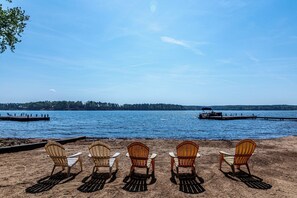 Relax on the lakeside beach with Adirondack chairs, a dock, and a serene view.