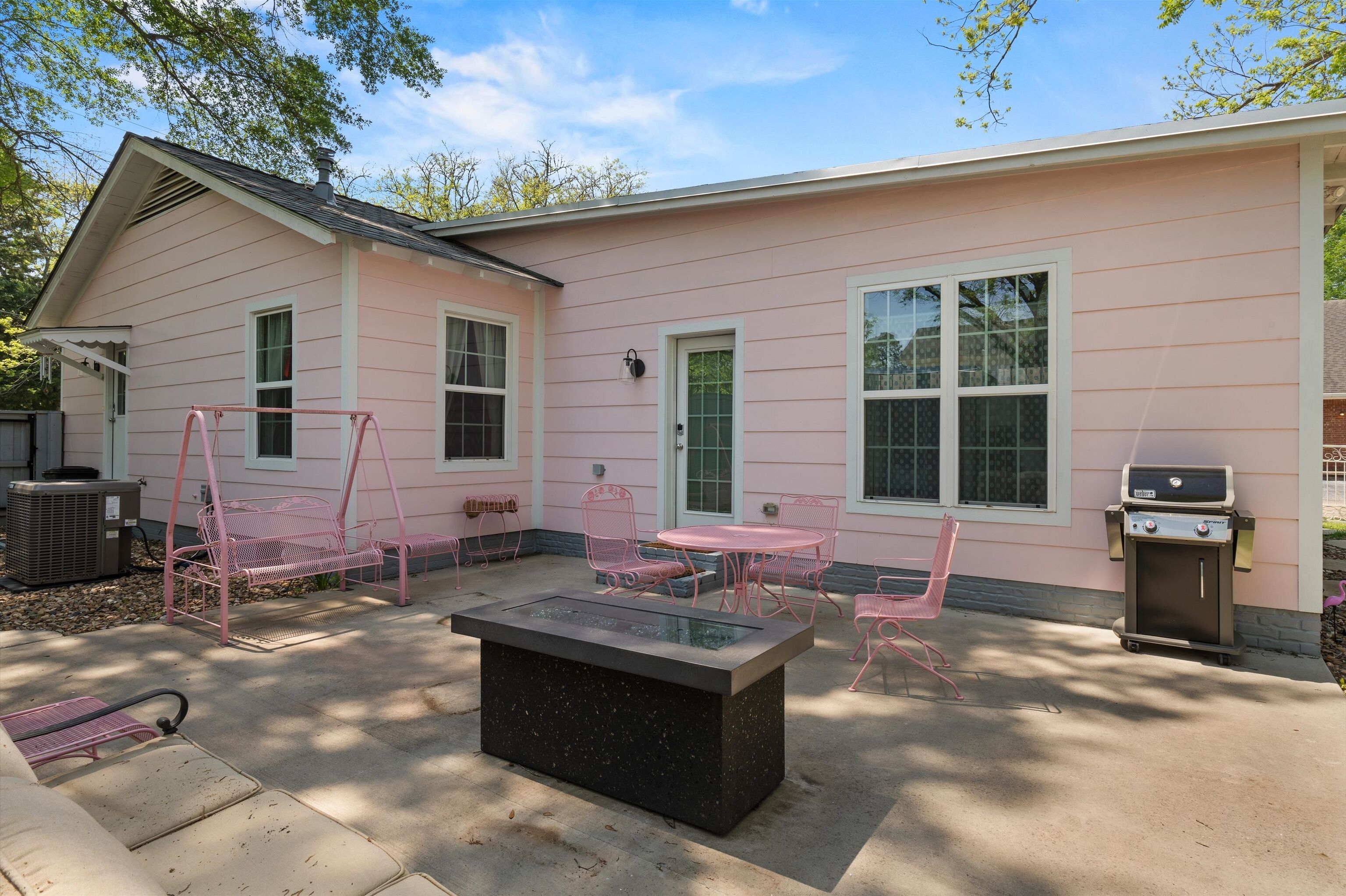 Une maison rose avec un patio, un espace salon extérieur et un barbecue.