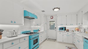 Una cocina con armarios blancos, una estufa azul y un microondas.