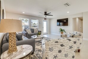 Una sala de estar con sofá, sillón, mesa de centro y televisión montada en la pared.