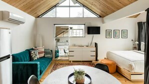 Una habitación moderna y compacta con techo inclinado, una mesa de comedor con un centro de mesa de plantas, un sofá, una cama y un escritorio con una computadora.