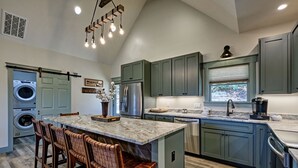 A modern kitchen with a central island, built-in appliances, and a large window. - The Owlery, Walk to Town (Highlands)