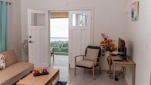 A modern living room with a sofa, a chair, a desk with a computer, and a view through a door to a balcony.