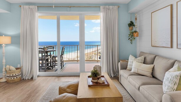 A living room with a view of the beach, a ceiling fan, and a sofa.