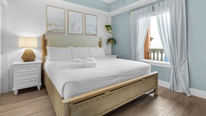 A bedroom with a wooden bed, white bedding, a bedside lamp, and framed artwork on the wall.