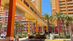 A multi-story hotel with a yellow facade, palm trees, and a clear blue sky.