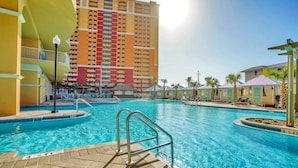 A hotel pool area with a large pool, a lifeguard stand, and a building with multiple balconies in the background.