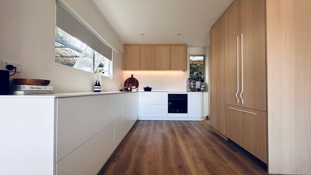 Une cuisine moderne avec des meubles blancs, un plancher en bois et une fenêtre qui laisse entrer la lumière naturelle.