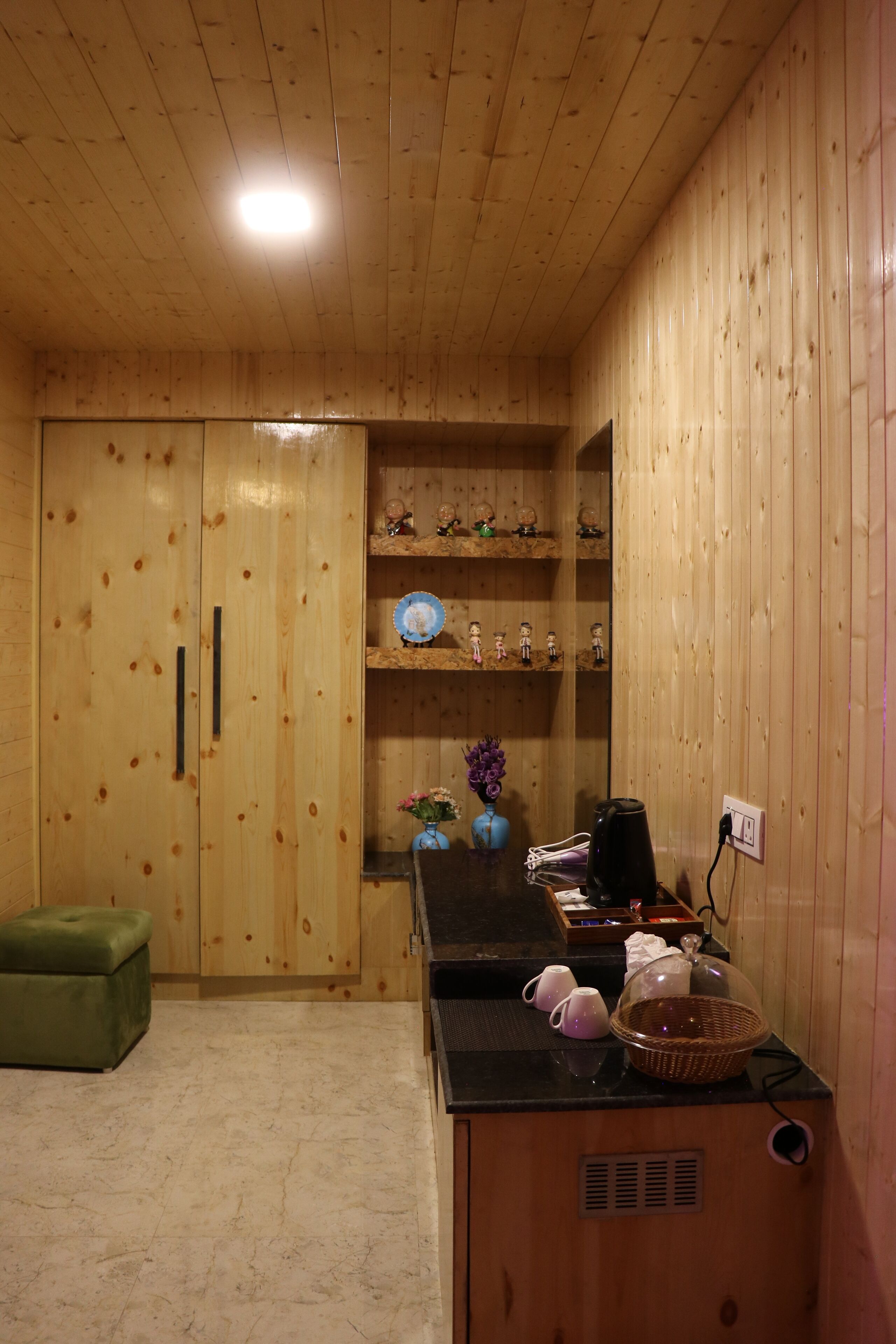 A wooden-paneled room with a cabinet, a small table with a basket, and a green ottoman.