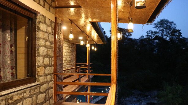 A stone building with a wooden staircase and railing, leading to a balcony with hanging lights. - SUKOON DK (Jakholi)