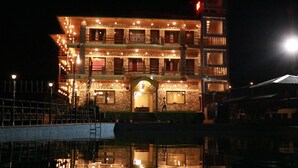 A multi-story building with a brick facade, multiple balconies, and a reflective pool in front. - SUKOON DK (Jakholi)
