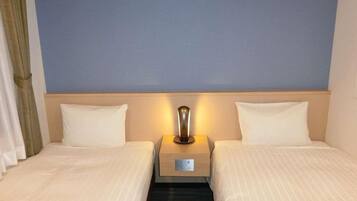 A hotel room with two beds, a nightstand with a lamp, and a plain blue wall.
