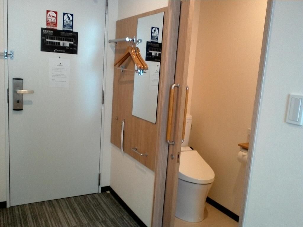 Una habitación de hotel con una puerta de madera, un inodoro blanco y un espejo.