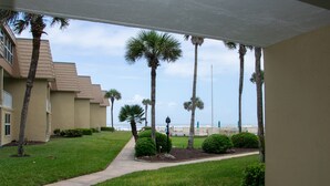 A pathway leading to a building with palm trees and a view of the ocean. - Coquina B101 Ground-Floor Coastal Condo (Saint Augustine)