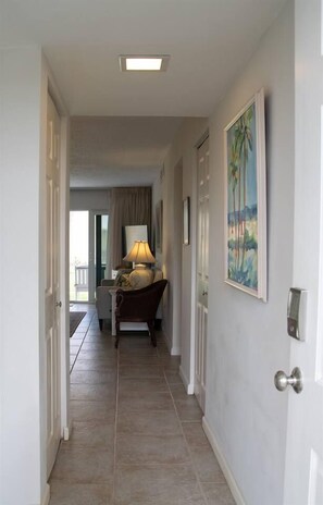 Un couloir avec une porte sur la droite, un tableau au mur et une lampe sur une table.