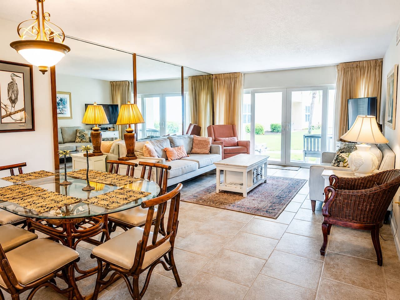 A spacious living area with a glass dining table, comfortable seating, and a large window offering a view of the outdoors.