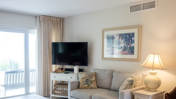 A living room with a sofa, a television, a lamp, a coffee table, and a patterned rug. - Coquina B101 Ground-Floor Coastal Condo (Saint Augustine)