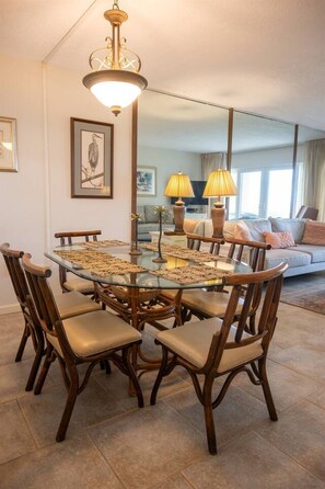 A dining area with a glass-top table surrounded by wooden chairs with cushioned seats. - Coquina B101 Ground-Floor Coastal Condo (Saint Augustine)
